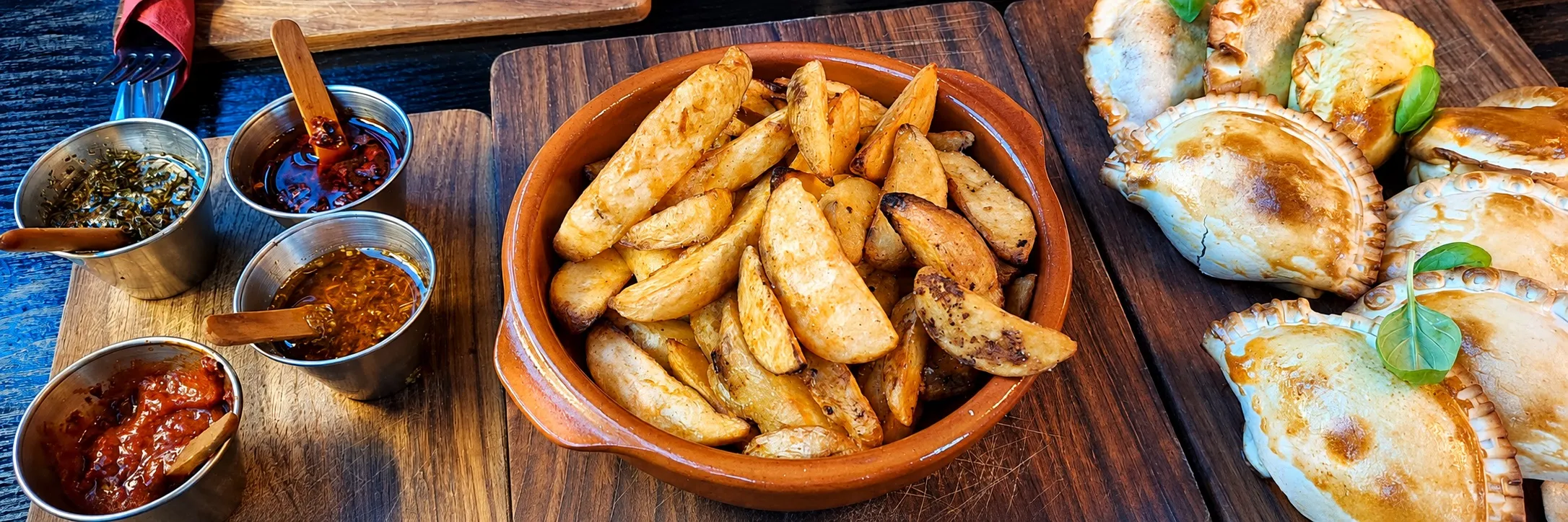 Empanadas, Wedges und hausgemachte Saucen auf dem Holzbrett
